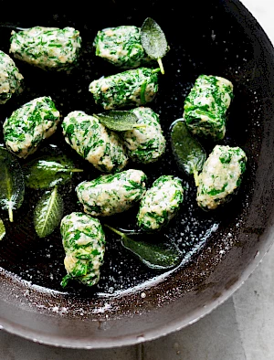 Photograph of a pan of homemade ricotta and spinach gnocchi with sage leaves in melted butter.