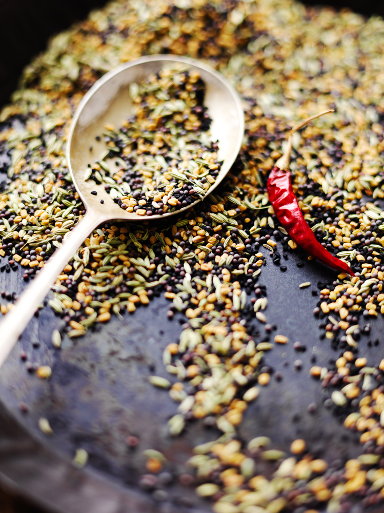 Photograph of dry spices being dry fried in a pan and a spoon with some of the spice mix