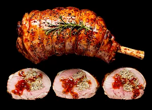 Photograph of whole roast leg of lamb with slices and redcurrant sauce and rosemary