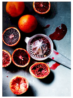 Photograph of blood oranges being juiced with metal hand juicer