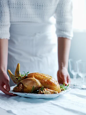 Person holding a platter of roast chicken and placing on a table.