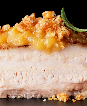 Photograph of roast pork belly with apple sauce topping and crumble with sage