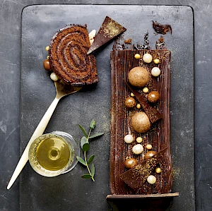 Photograph of Christmas chocolate log with chocolate balls of white, milk and dark chocolate with slice