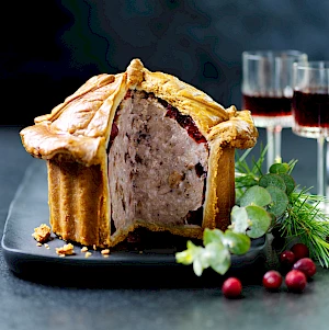 Photograph of a Christmas Tudor Pie with glasses of red wine, cranberries, pine and eucalyptus propping