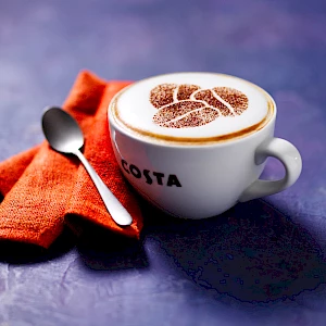 Photograph of a flat white in a cup with orange napkin on purple background